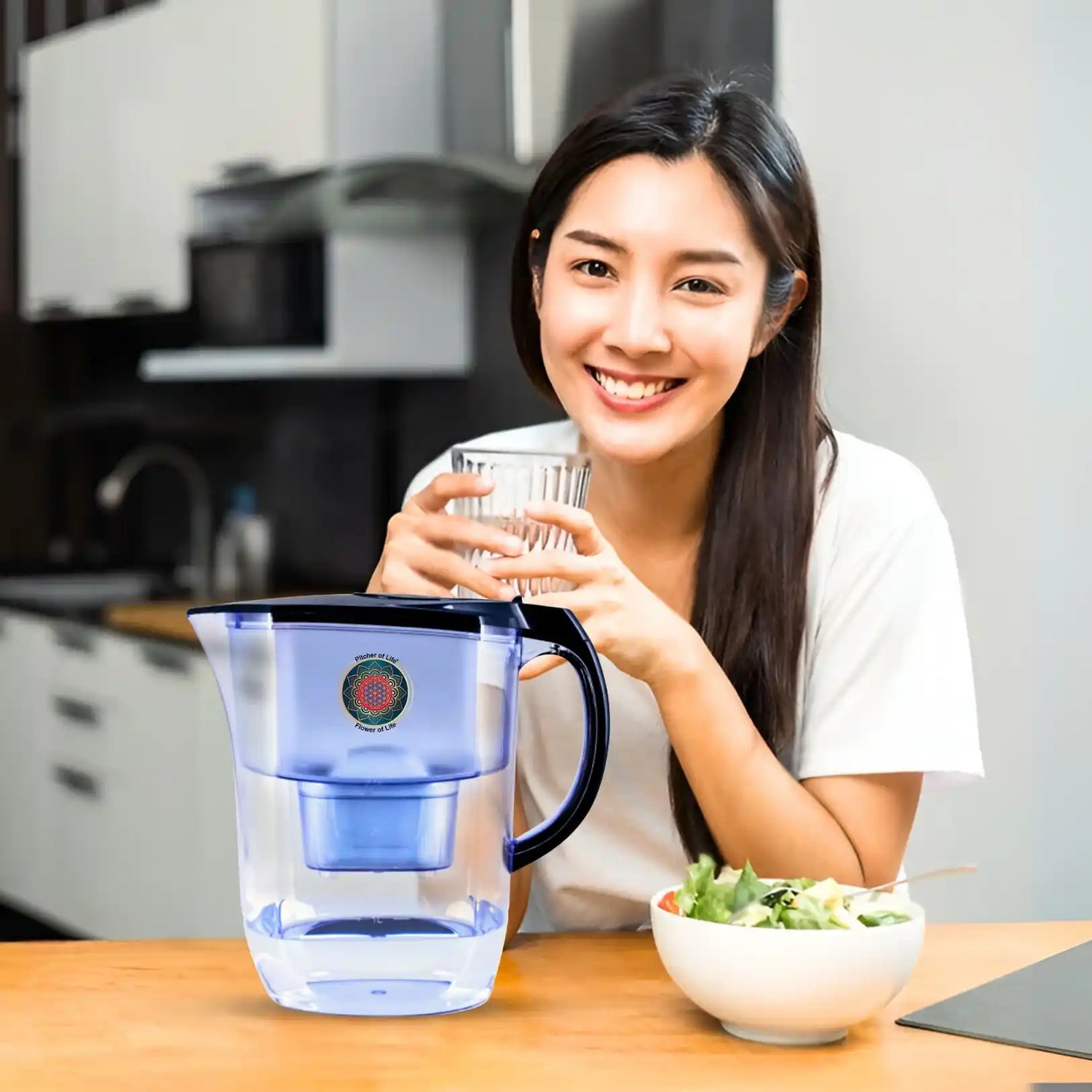 Woman holding a glass of water next to a blue water pitcher in a kitchen.