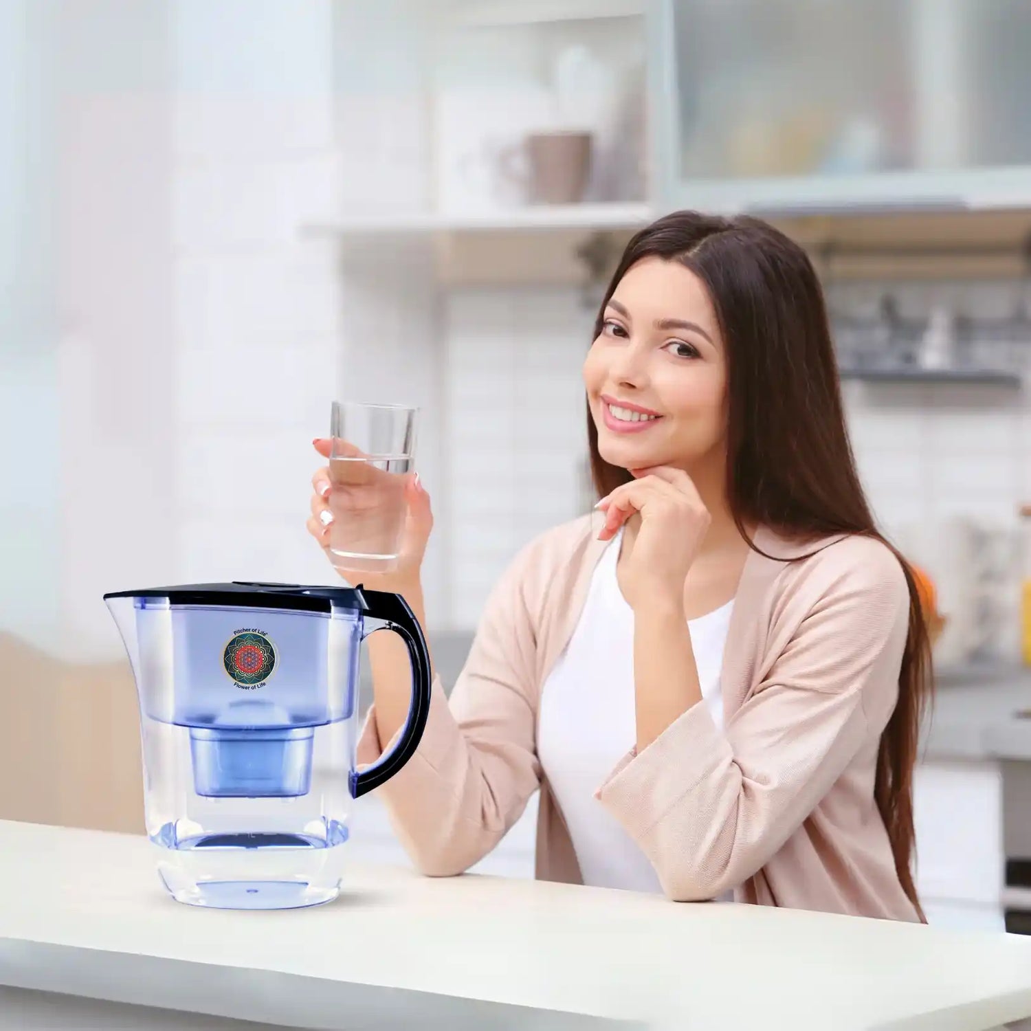 Woman holding a glass of water next to a water filter pitcher in a kitchen.