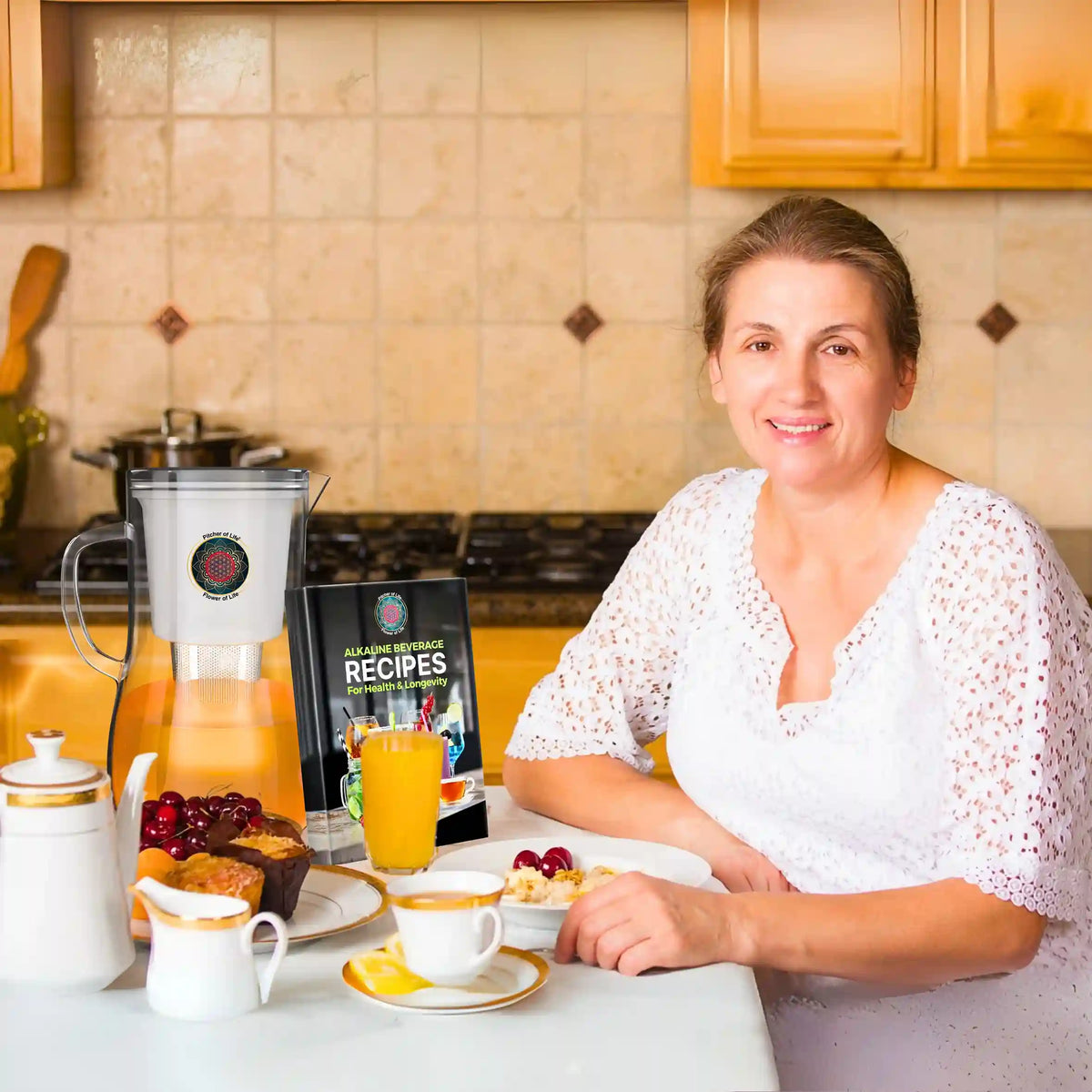 Woman drinking orange juice from a glass in a kitchen with a pitcher of juice on the counter.